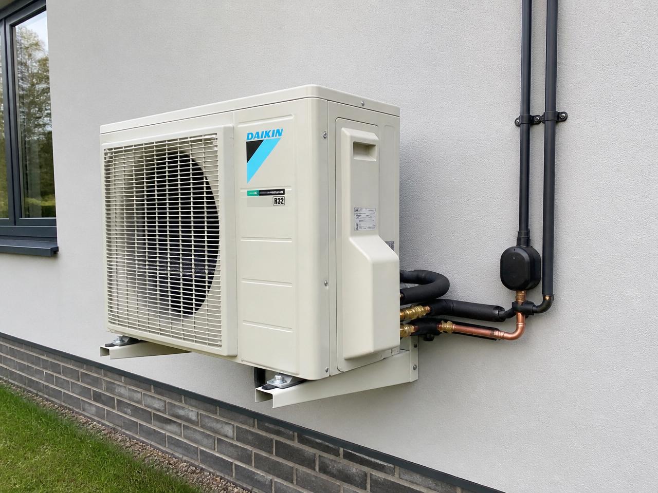 Outdoor air conditioning condenser unit mounted on a brick wall with refrigerant pipework